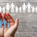Paper family in hands on wooden background with white families